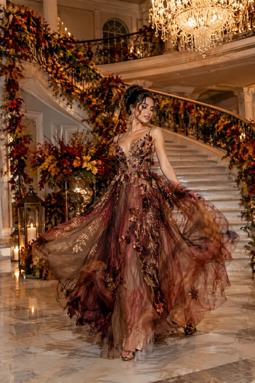 A flowing burgundy and brown tulle gown with floral embellishment and a deep V neckline, styled with drop earrings and open-toe heels.