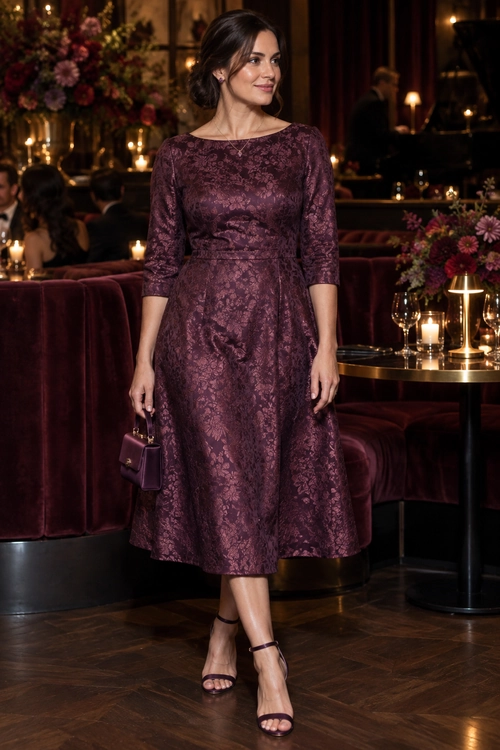 Burgundy Floral Midi Dress A woman wears a burgundy floral-patterned midi dress with three-quarter sleeves, a small purple handbag, and strappy heeled sandals.