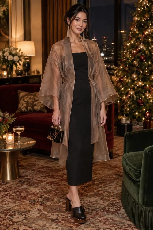 A black strapless midi dress is layered with a sheer taupe wrap and styled with drop earrings, a small black clutch, and chunky black heels.