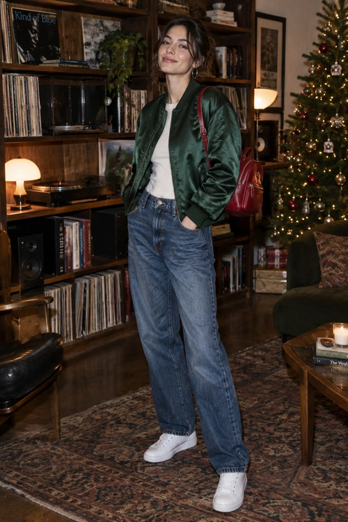 Green Bomber Jacket and Jeans A green bomber jacket over a white top with blue jeans, white sneakers, a red backpack, and hoop earrings.