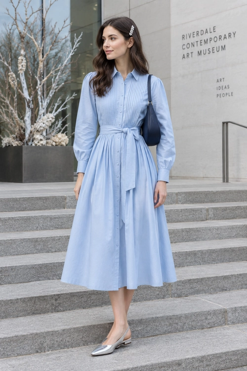 Light Blue Belted Shirt Dress A light blue button-front shirt dress with a tied waist, silver flats, and a dark shoulder bag.