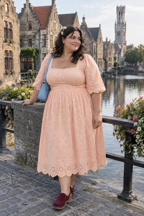 A peach eyelet midi dress with flutter sleeves is paired with a light blue shoulder bag and burgundy clogs.