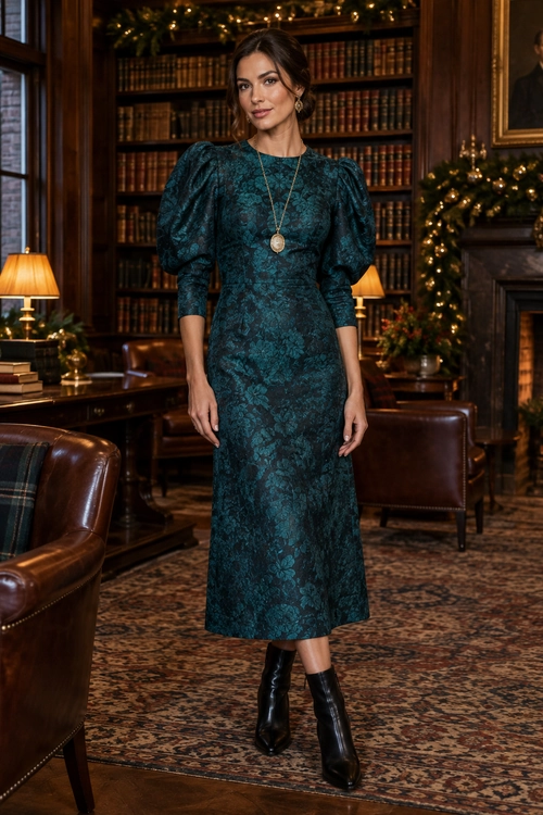 A dark teal floral midi dress with puff sleeves is styled with black ankle boots and a long pendant necklace.